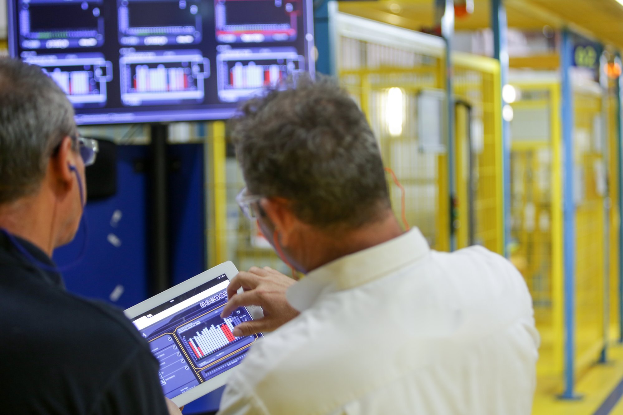 Production managers reviewing Visual Factories OEE data on a tablet under the floor monitor